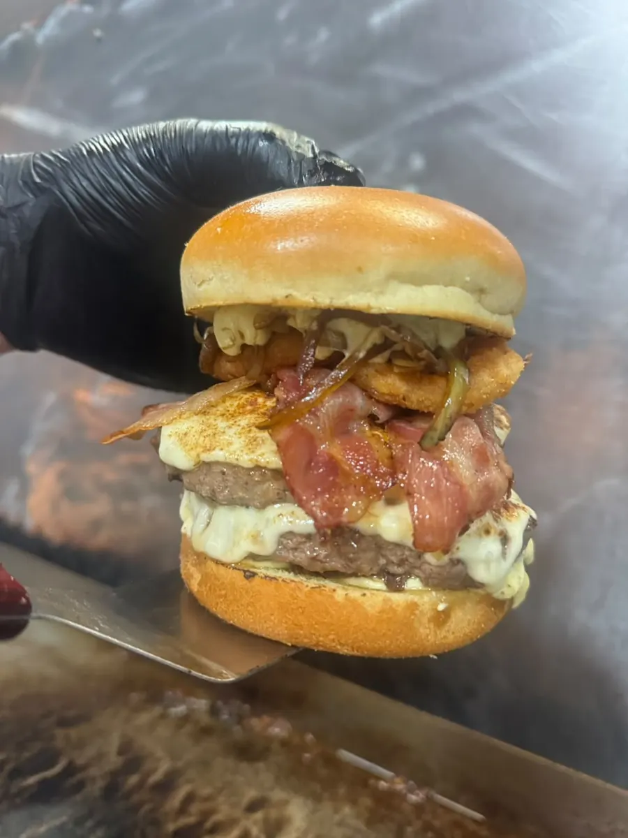 Hambúrguer duplo com bacon e anéis de cebola saindo da chapa